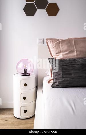 Particolare della testata di una camera da letto con comodino cilindrico a tre cassetti e cuscini sulla testata del letto Foto Stock