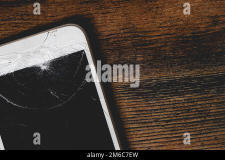 Primo piano di un telefono cellulare danneggiato con schermo incrinato per la riparazione su uno sfondo di legno con spazio copia Foto Stock