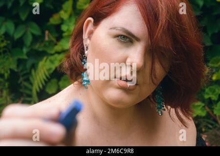 Primo piano ritratto della giovane latina caucasica ispanica, donna argentina rossa con occhi verdi, puntando la fotocamera con un gesso e tenendo la c Foto Stock