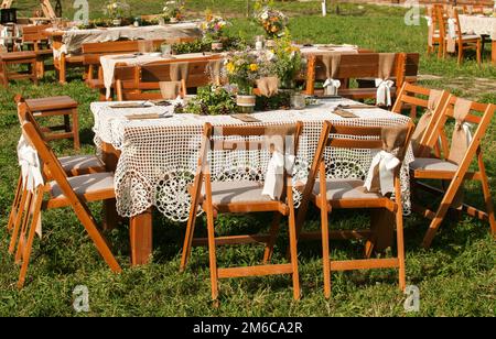 Tavoli impilati per gli ospiti per la cerimonia di matrimonio rustico all'aperto di prato verde in casa di campagna gar Foto Stock