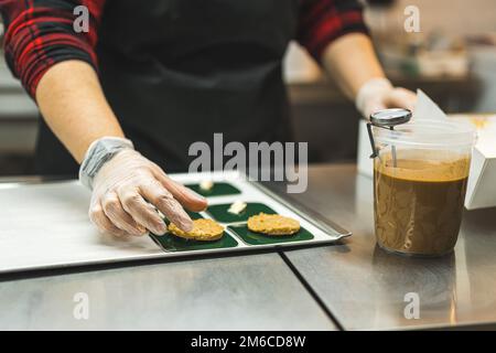 Baker posizionare i biscotti su piastre quadrate verdi su una teglia da forno Inforna la glassa in una tazza di plastica posta accanto alla teglia da forno Foto di alta qualità Foto Stock