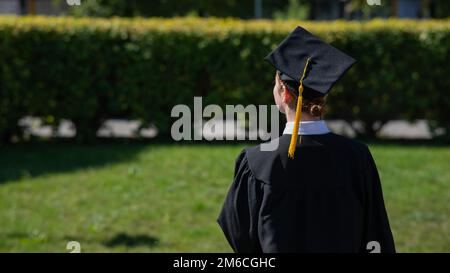 Una donna lancia il suo cappellino di laurea contro il cielo blu. Foto Stock