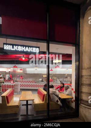 Strasburgo, Francia - 11 novembre 2022: Scena di strada con le donne asiatiche etnicità che parlano al tavolo di legno all'interno del ristorante fast food Five Guys Foto Stock