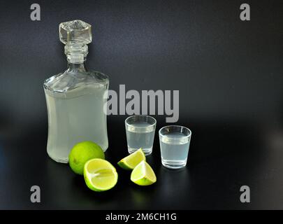 Liquore di lime su fondo nero, una bottiglia e due bicchieri con alcol fatto in casa, accanto a pezzi di agrumi maturi. Primo piano. Foto Stock