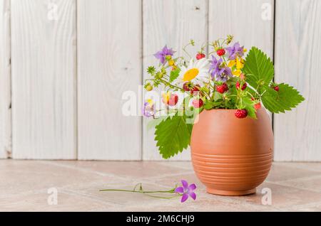 Fragole mature e un mazzo di fiori di bosco in una tazza di argilla Foto Stock