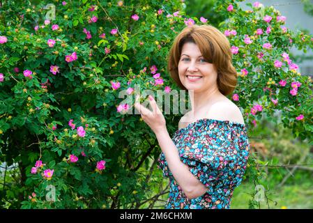 Donna sorridente in piedi vicino a fioritura rosa canina Foto Stock