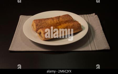 Due panini con salsiccia. Su un piatto bianco e tovaglia grigia. Su sfondo nero. In prospettiva Foto Stock