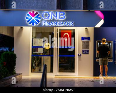 Banche turche - QNB Finansbank - edifici colorati in banca illuminati. Kadikoy Istanbul Turchia. Giovane uomo che ritira denaro in ATM Foto Stock