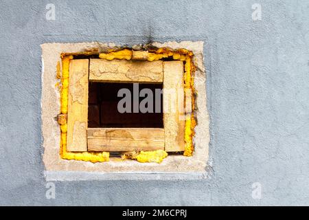 Un foro quadrato con blocchi di legno in una parete di mattoni dipinta con vernice grigia. Foto Stock