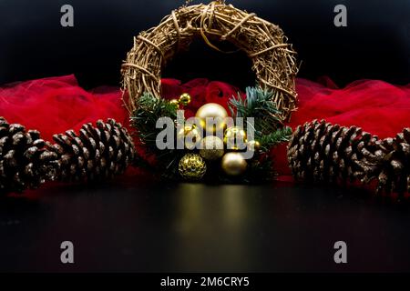 Corona di Natale e coni di pino con tessuto rosso sul nero. Foto Stock