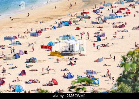 Turisti e turisti che prendono il sole e si godono il tempo estivo alla spiaggia di Porthminster con RNLI Lifeguard Hut al centro, St Ives, Cornwall, Regno Unito. Foto Stock