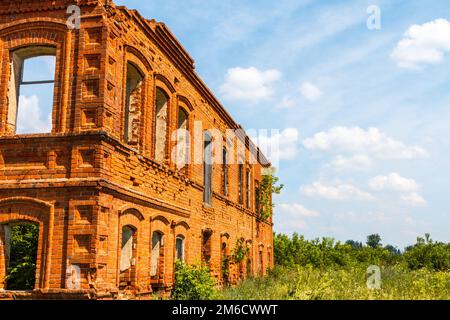 Una grande casa in rovina antica di mattoni rossi contro un cielo blu con nuvole bianche. Foto Stock