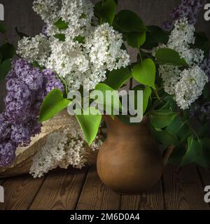 Still-life con un mazzo di lillà e un cappello di paglia Foto Stock