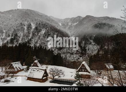 Tradizionale villaggio giapponese e montagne coperte di neve nebbiosa in inverno Foto Stock