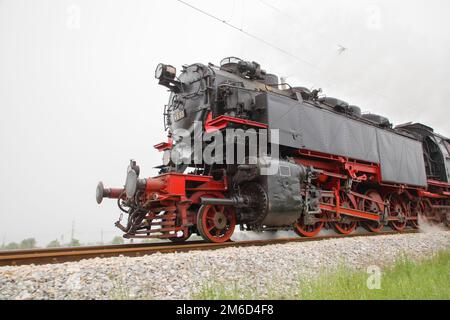 Vintage vapore locomotiva a motore accelerando sui binari della ferrovia di curva e soffia forte emissione di fumo bianco. Foto Stock