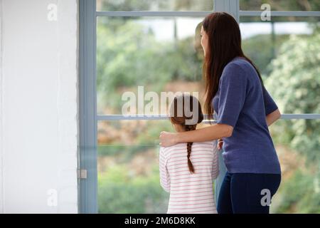 Momenti speciali con la mamma. Ripresa da dietro di una madre e una figlia amorevoli che guardano fuori dalla finestra. Foto Stock