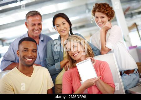 Guarda il nostro sito. Ritratto di un gruppo eterogeneo di colleghi che ti mostra un tablet digitale in un ambiente di ufficio informale. Foto Stock