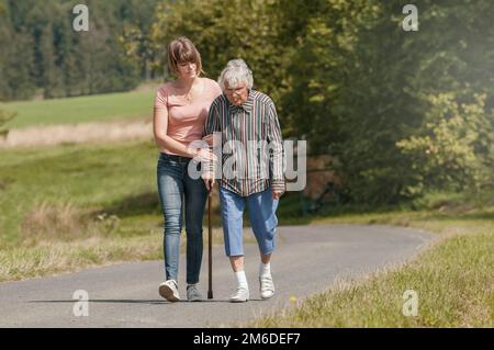 Giovane donna aiuta donna senior a piedi con bastone Foto Stock