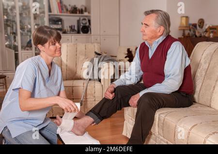 Caregiver che lega il piede dell'uomo anziano Foto Stock