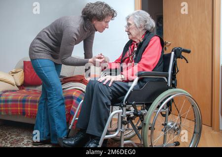 Donna anziana seduta in sedia a rotelle con operatore sanitario Foto Stock