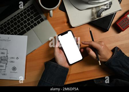 Vista dall'alto delle mani dell'ingegnere che tiene lo smartphone sopra la sua workstation. Schermo vuoto per la pubblicità Foto Stock