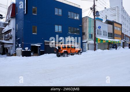 Hokkaido, Giappone - 19 dicembre 2022 : Un'elegante jeep arancione è parcheggiata sulla strada coperta di neve a Hokkaido Foto Stock