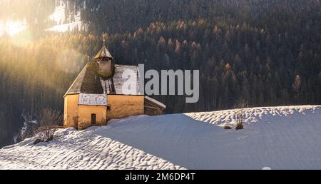 Paesaggio montano, pendio di neve panoramico con chiesa in inverno giorno con sole e lente flare Foto Stock