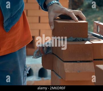 Un uomo costruisce un muro di mattoni. Mattone messo sulla soluzione. Costruzione di casa di mattoni. Foto Stock