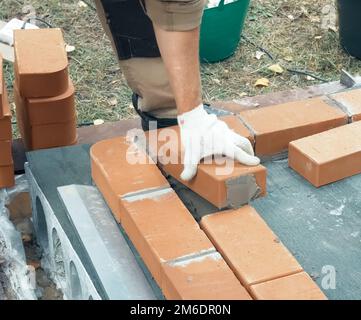 Un uomo costruisce un muro di mattoni. Mattone messo sulla soluzione. Costruzione di casa di mattoni. Foto Stock