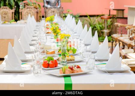 Tavolo lungo servito con piatti, bicchieri, tovaglioli, sedie e piatti Foto Stock