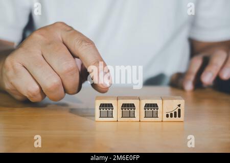 Business cubo blog di legno con l'icona del negozio di vendita in franchising. Mano dell'uomo d'affari che sceglie l'icona del grafico per la crescita di affari, commercio di franchising e suc Foto Stock