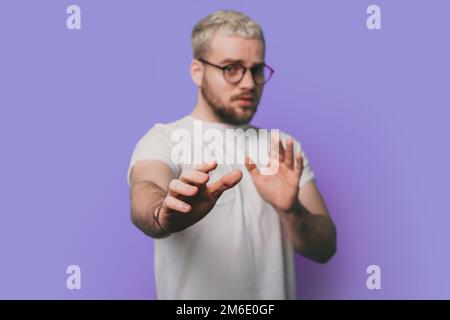 Uomo caucasico indossando occhiali che fanno espressione di disgusto perché reazione di avversione, in piedi con le mani sollevate isolato su sfondo viola. Foto Stock