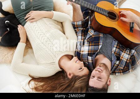 HES così un romantico senza speranza. un giovane che suona la chitarra mentre si sdraia sul pavimento con la sua ragazza. Foto Stock