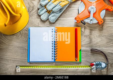 Composizione di guanti di sicurezza per notebook con nastro di misurazione, elmetto su asse di legno. Foto Stock