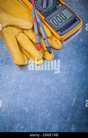 Guanti di protezione per tester elettrici digitali su sfondo metallico. Foto Stock