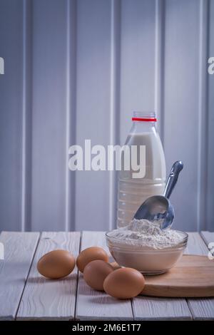 farina di uova in ciotola scoopop bottiglia di latte su bianco dipinto vecchio legno tavola concetto di cibo e bevande Foto Stock