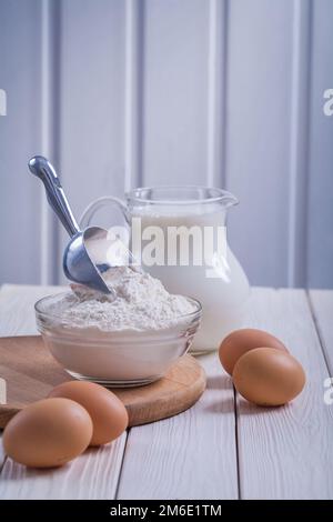farina di uova in caraffa ciotola trasparente con latte su vecchio legno dipinto di bianco cibo e bevande concetto Foto Stock