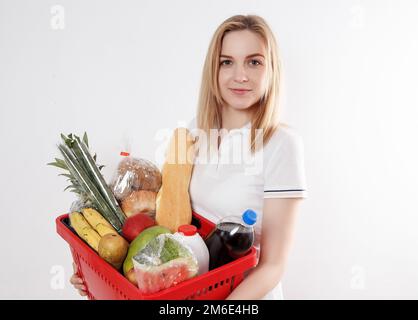 Giovane donna con prodotti nel cestino. Ragazza che tiene un cestino di generi alimentari. Verdure, frutta, biscotti, latte nel cestino della drogheria. Foto Stock