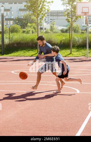 Papà e figlio giocano a basket a piedi nudi in un parco giochi Foto Stock