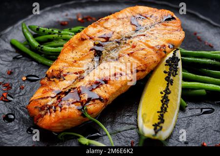 Bistecca di salmone alla griglia con asparagi e limone su un piatto nero Foto Stock