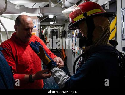 OCEANO INDIANO (26 aprile 2022) danni Controlman Fireman Nicholas Rozanski, a sinistra, aiuta danni Controlman 3rd Classe Amber Burnett con indossare guanti antincendio durante un trapano di controllo danni a bordo del cacciatorpediniere missile guidato USS Gridley (DDG 101) nell'Oceano Indiano, aprile 26. Gridley è dislocato nell'area operativa della flotta degli Stati Uniti 5th per garantire la sicurezza e la stabilità marittima nella regione del Medio Oriente. Foto Stock