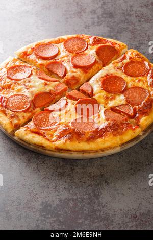 Pizza calda pepperoni fatta in casa pronta a mangiare da vicino su un asse di legno sul tavolo. Verticale Foto Stock