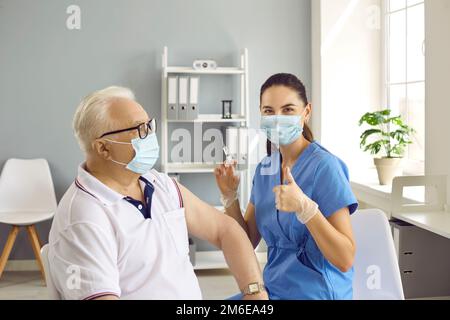Medico che prepara la siringa per vaccinare il paziente anziano e fare il gesto del pollice Foto Stock