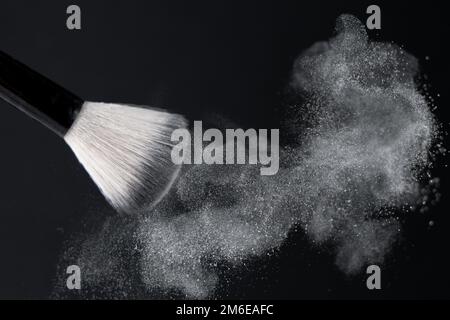 Spazzola per il trucco con polvere galleggiante bianca schiacciata su sfondo nero Foto Stock