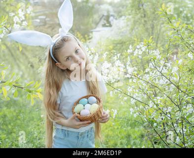 Grazioso fanciullo indossando orecchie di coniglietto il giorno di Pasqua. Ragazza con cesto con uova dipinte. Foto Stock