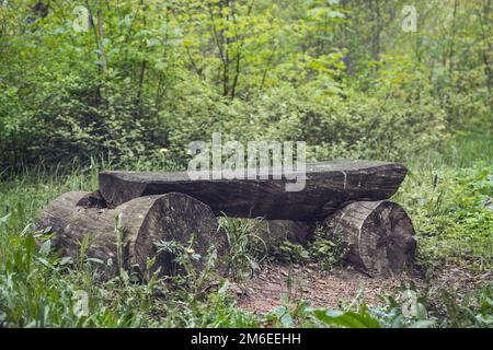 Panca in legno d'epoca realizzata in materiali naturali nella parte ombreggiata del giardino o del parco, all'aperto. Panca vuota sotto un albero nel parco, un bene Foto Stock