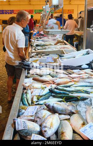 Clienti che guardano il pesce fresco su ghiaccio in una bancarella di cibo locale. Al mercato di Tavira, Mercado a Tavira, Algarve, Portogallo, Europa. Foto Stock