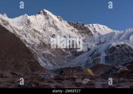 Concetto di campeggio esterno estremo. Campeggio invernale in montagna. Tenda solitaria nella valle sotto la montagna di Cho Oyu in serata, Himalaya, Nepal Foto Stock