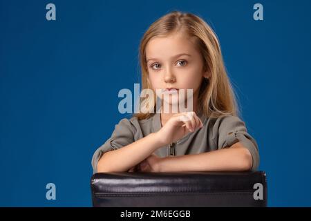Una bambina con gli occhi grigi e i capelli biondi siede su una sedia Foto Stock