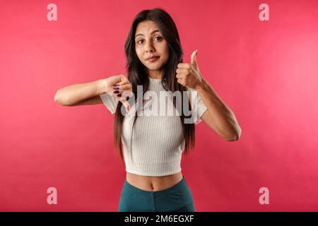 Giovane bella donna che indossa il raccolto a coste isolato su sfondo rosso facendo pollici su e giù, disaccordo ed espressione di accordo. Sembra unsu Foto Stock